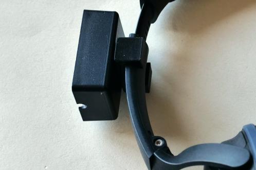 A small black plastic enclosure mounted to a headphone via a 3D-printed C-clamp