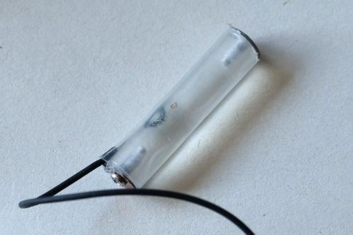 A piece of acrylic rod with wires soldered to small pieces of copper, all covered in heatshrink to serve as a dummy battery for a Bose QuietComfort 25 headphone