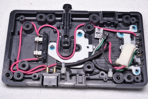 Een zwart plastic plaat met bedrading en metalen onderdelen, een V-mount accuplaat van IDX