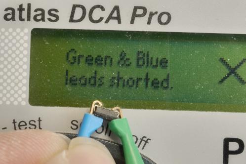 Een blauw en groen meetklemmetje met daartussen geklemd een SMD diode, met een groen LCD dat toont dat groen en blauw kortgesloten zijn, defecte diode uit een Tristar 4 ledlampje