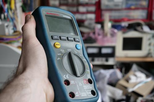 Een donkergrijs en blauwe hand-multimeter in uitgeschakelde toestand, met zicht op het LCD, een Multimetrix DMM220 digitale multimeter