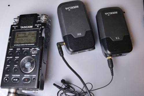 Twee kleine zwarte kastjes met draden en een grotere zwarte kast, een Rodelink Filmmaker TX en RX unit en Tascam DR-100 V2