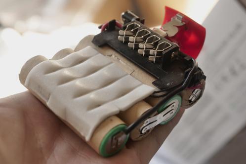 4 cilindrische lithiumcellen met extra karton-isolatie en wit schuim en zonder enige beveiligings-elektronica, met de metalen aansluitklemmen zichtbaar, een geopende Bosch PSR lithium schroefmachine-accu