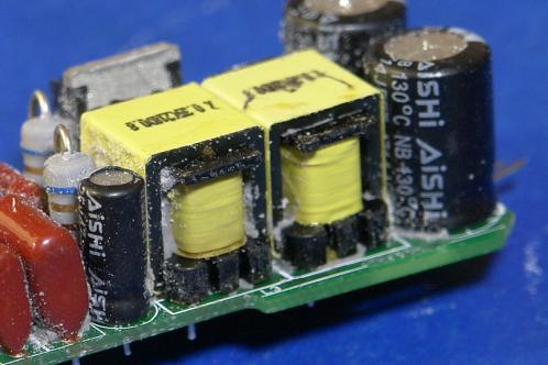 Een duidelijker close-up van twee zwarte cilindrische condensatoren (elco's) gemerkt met 'Aishi op de elektronicaprint van een Osram AC01754 LEDlamp