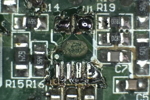 Een microscoopfoto van een groene elektronicaprint van de plek waar een IW3689-01 SOIC-8 IC gezeten heeft, na verwijdering ervan. Het teveel aan tin en de Bruine fluxresten moeten nog verwijderd worden