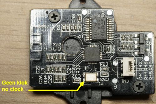 Een kleine zwarte printplaat met uitsluitend SMD-onderdelen in 0402 formaat, twee IC's, een antenne klok-oscillator en connector voor verbinding met een andere print, de ontvangstmodule met A7105 IC van een Patona DMW-BGGH5RC batterygrip met de uitgang van de klok-oscillator, pin 3, gemarkeerd
