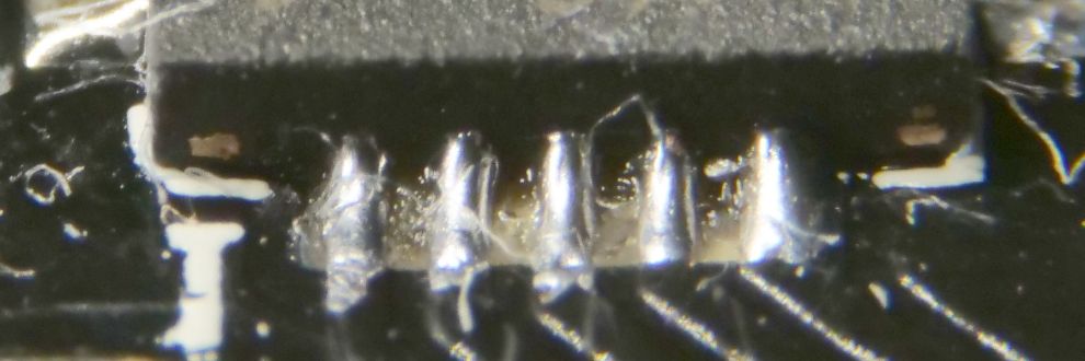 De zijkant van een IC (A7105) in QFN behuizing met zicht op de eerste 5 pinnen na hersolderen, waar nu mooie tinverbindingen zichtbaar zijn