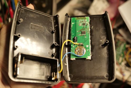 Een zwarte, plastic behuizing bestaande uit twee helften getoond in geopende toestand, met binnenin een kleine groene printplaat en wat bedrading dat naar een batterijvak voor 2 AA batterijen loopt, een nieuwe behuizing voor de Patona DMW-BGGH5RC batterygrip afstandsbediening