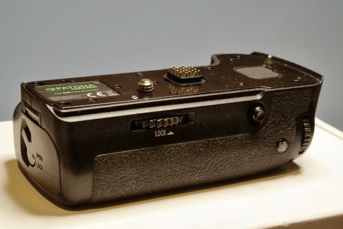 Een glooiend zwart plastic onderdeel met gouden pogo-pinnen op de bovenkant en een schroef met statiefschroefdraad ter montage aan een fotocamera, een Patona DMW-BGGH5RC batterygrip