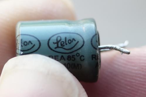 Een cilindrische elektrolytische condensator met twee pootjes, voorzien van een groene krimphuls met daarop in zwarte letters de naam van de fabrikant 'Lelon'