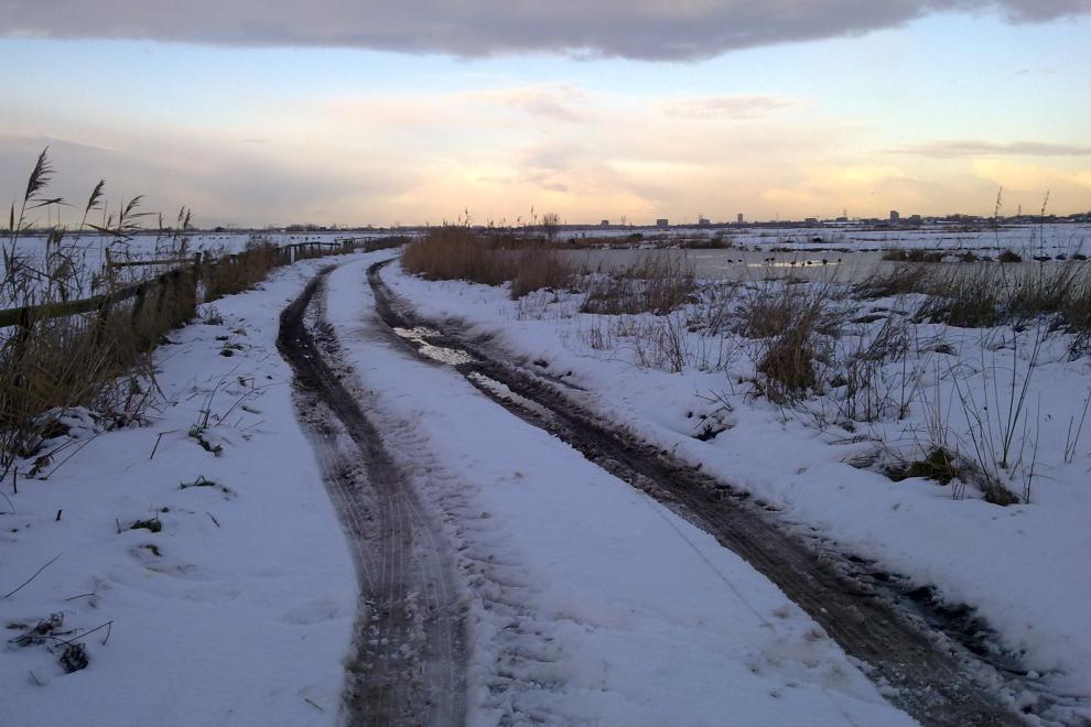 Zon en bewolking schijnen over boerenvelden bij Purmerland, waar een modderig tractorpad naar de horizon loopt, temidden van door sneeuw bedekte velden op 12 december 2017