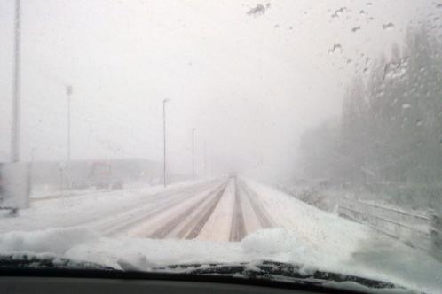 Zicht vanuit een auto op nauwelijks zichtbare rijbaan, door sneeuw bedekte bomen en verzamelende sneeuw op voorruit van auto tijdens sneeuwjacht op de Noorder IJ- en Zeedijk op 11 december 2017
