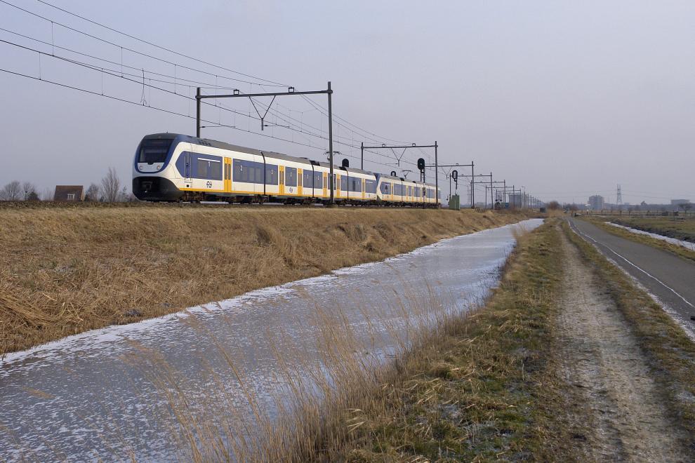 Een trein rijdt voorbij ter hoogte van Purmerland op een nevelige dag. De sloot naast de spoordijk is bevroren en gedeeltelijk bedekt door flarden poedersneeuw