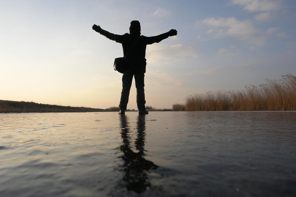 Zelfportret met tegenlicht. De camera staat op de ijsvloer en ik sta met open armen, waarbij ik slechts een silhouet ben, op het ijs van de Ringvaart in het Twiske